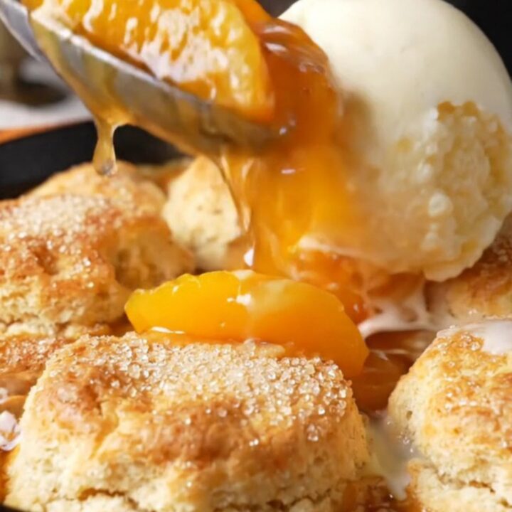 Cast iron skillet filled with bubbling peach cobbler topped with golden biscuits
