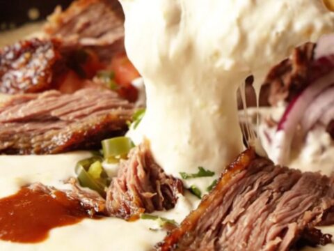Cast iron skillet filled with bubbling white queso dip, chunks of smoked brisket, and a swirl of barbecue sauce