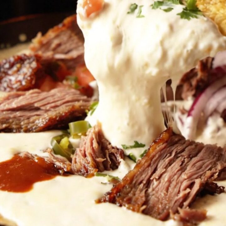 Cast iron skillet filled with bubbling white queso dip, chunks of smoked brisket, and a swirl of barbecue sauce