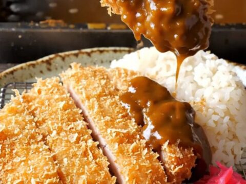 Golden chicken katsu cutlet sliced and laid beside steamed rice with dark curry sauce and pickled radish