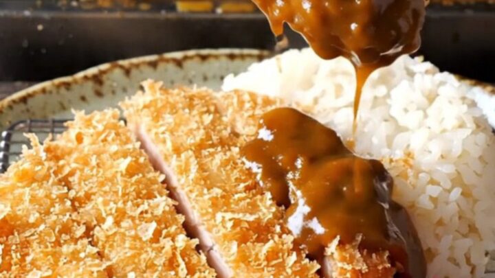 Golden chicken katsu cutlet sliced and laid beside steamed rice with dark curry sauce and pickled radish
