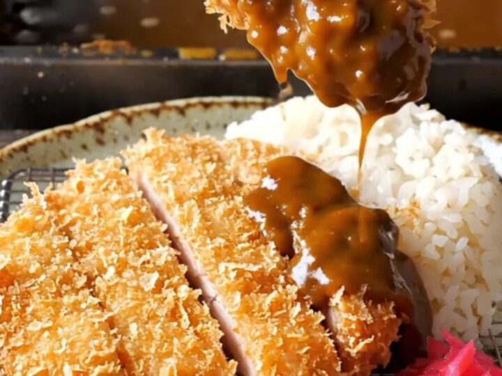 Golden chicken katsu cutlet sliced and laid beside steamed rice with dark curry sauce and pickled radish