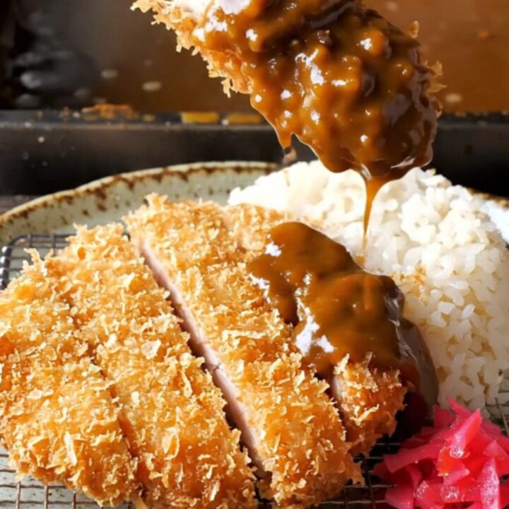 Golden chicken katsu cutlet sliced and laid beside steamed rice with dark curry sauce and pickled radish