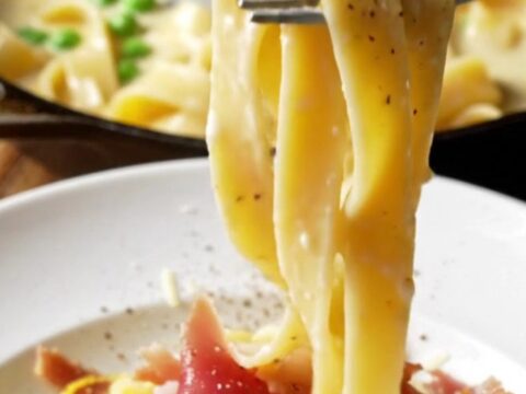 Overhead shot of creamy lemon ricotta pappardelle in a skillet, topped with crispy prosciutto and peas.