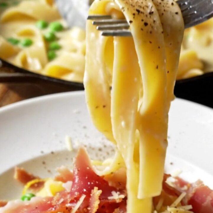 Overhead shot of creamy lemon ricotta pappardelle in a skillet, topped with crispy prosciutto and peas.