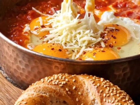 Copper pan filled with menemen, topped with melted kaşar cheese and a piece of simit dipping in