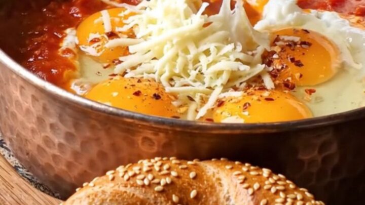 Copper pan filled with menemen, topped with melted kaşar cheese and a piece of simit dipping in