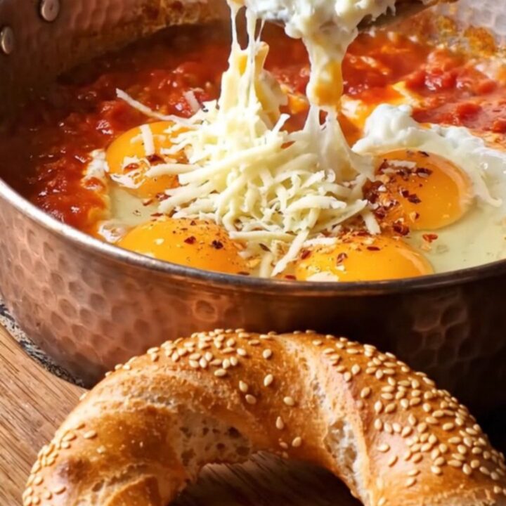 Copper pan filled with menemen, topped with melted kaşar cheese and a piece of simit dipping in