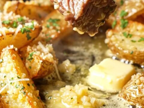 Garlic butter steak strips and parmesan potato wedges in a skillet, garnished with parsley.