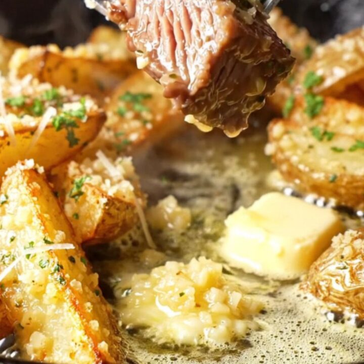 Garlic butter steak strips and parmesan potato wedges in a skillet, garnished with parsley.