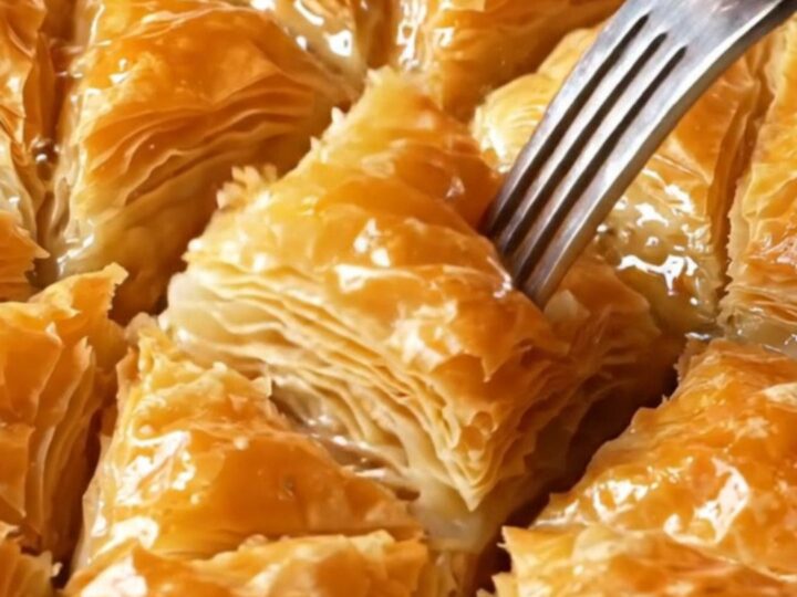 Golden diamond-cut Turkish baklava with syrup being poured over, showing flaky layers