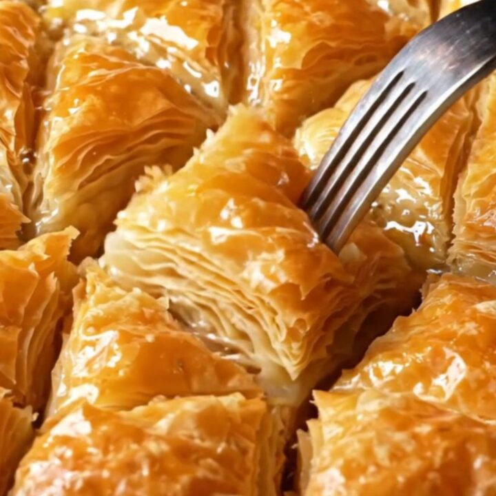 Golden diamond-cut Turkish baklava with syrup being poured over, showing flaky layers