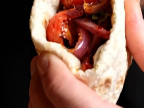 Grilled chicken shish wrap with sumac onions and peppers, cut in half on a wooden board