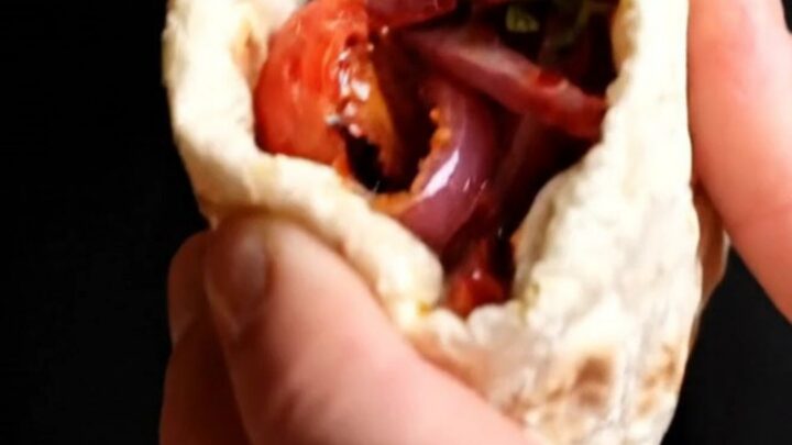 Grilled chicken shish wrap with sumac onions and peppers, cut in half on a wooden board