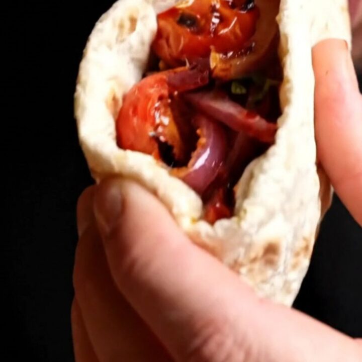 Grilled chicken shish wrap with sumac onions and peppers, cut in half on a wooden board