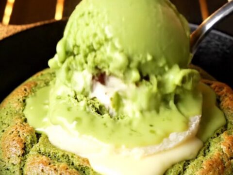 Molten white chocolate matcha skillet cookie with a spoon cracking open the center, lava flowing out