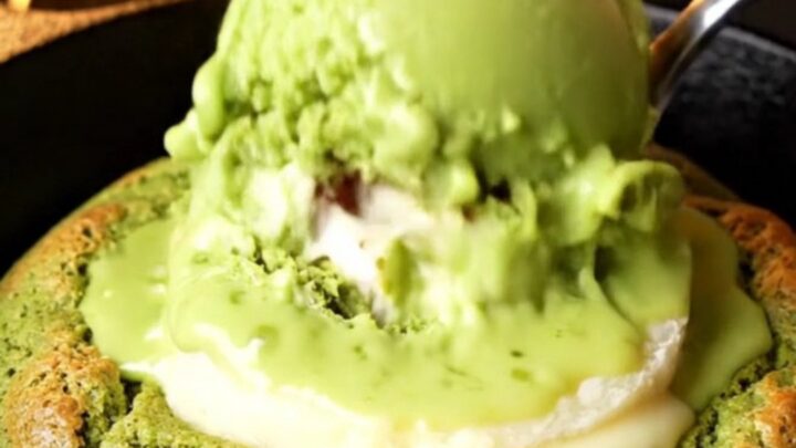 Molten white chocolate matcha skillet cookie with a spoon cracking open the center, lava flowing out