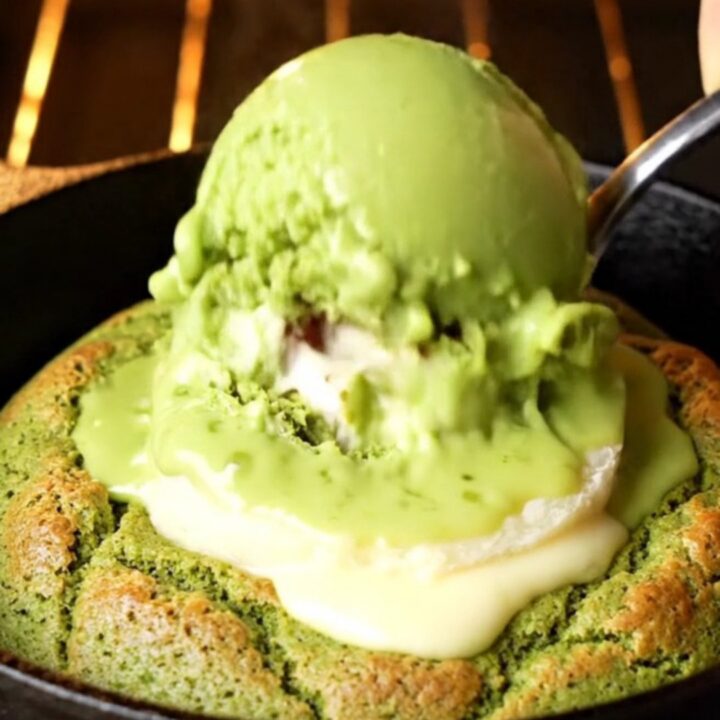 Molten white chocolate matcha skillet cookie with a spoon cracking open the center, lava flowing out