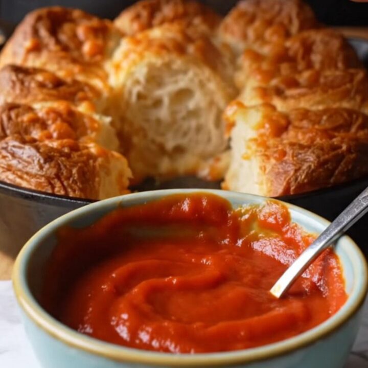 Golden pull-apart monkey bread in a cast iron skillet with melted cheese stretching between pieces.