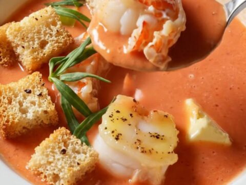 Creamy lobster bisque in a wide porcelain bowl, topped with butter-poached lobster medallions and garlic croutons.