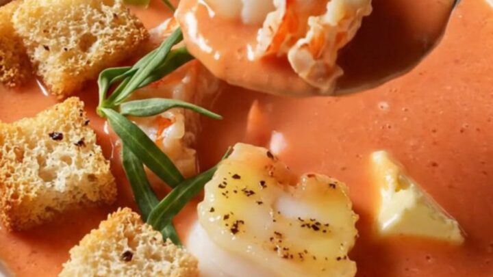 Creamy lobster bisque in a wide porcelain bowl, topped with butter-poached lobster medallions and garlic croutons.