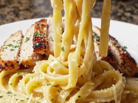 Creamy blackened chicken fettuccine Alfredo in a cast iron skillet, topped with sliced chicken and parsley.