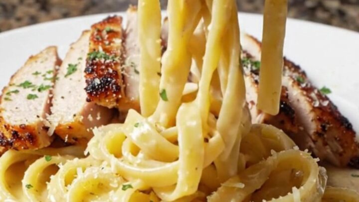Creamy blackened chicken fettuccine Alfredo in a cast iron skillet, topped with sliced chicken and parsley.