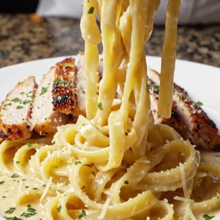 Creamy blackened chicken fettuccine Alfredo in a cast iron skillet, topped with sliced chicken and parsley.