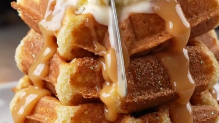 Stack of crispy churro waffles topped with vanilla ice cream and warm dulce de leche cascading down the sides.