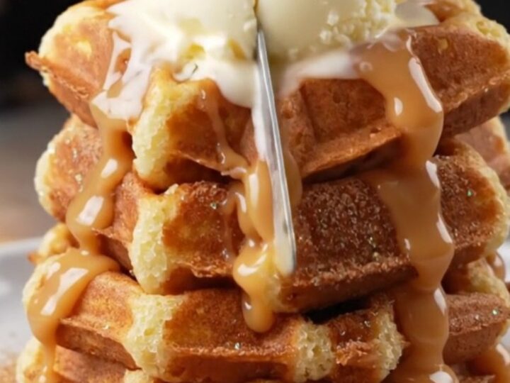 Stack of crispy churro waffles topped with vanilla ice cream and warm dulce de leche cascading down the sides.