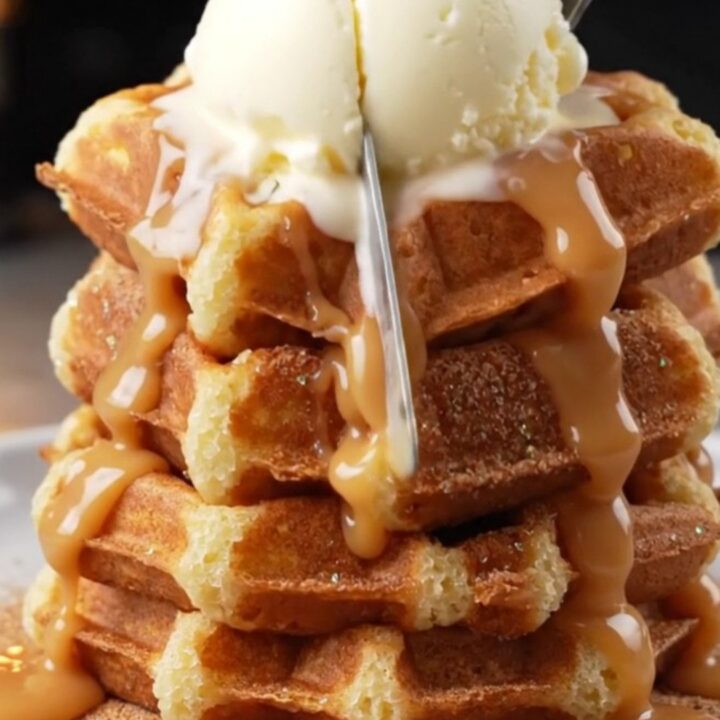 Stack of crispy churro waffles topped with vanilla ice cream and warm dulce de leche cascading down the sides.