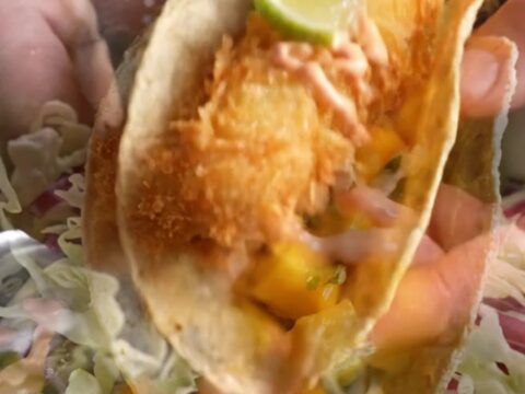 Golden beer-battered fish taco with mango slaw and chipotle crema on a corn tortilla