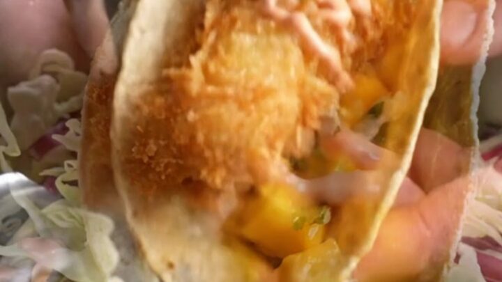 Golden beer-battered fish taco with mango slaw and chipotle crema on a corn tortilla