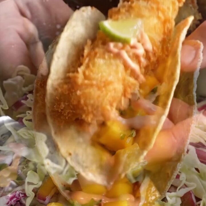 Golden beer-battered fish taco with mango slaw and chipotle crema on a corn tortilla