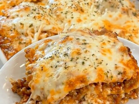 A golden-brown baked ravioli casserole in a white dish with steam rising from a freshly cut slice