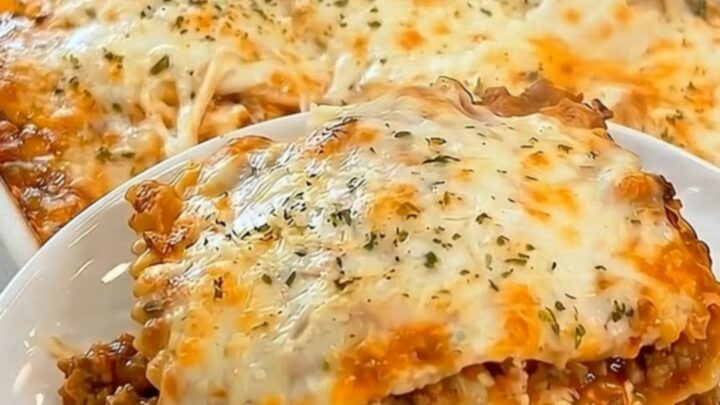 A golden-brown baked ravioli casserole in a white dish with steam rising from a freshly cut slice