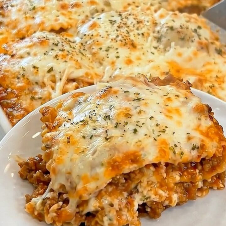 A golden-brown baked ravioli casserole in a white dish with steam rising from a freshly cut slice