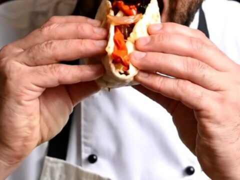 Turkish Adana kebab dürüm wrapped in lavash with charred peppers and sumac onions, cut in half, on a wooden board.
