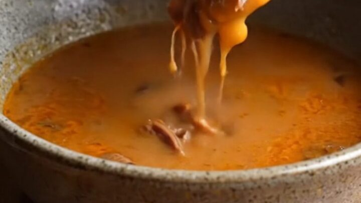 Crispy birria quesadilla on a cutting board, sliced to show melted cheese and shredded beef, with a bowl of consommé