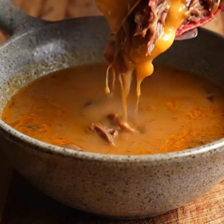 Crispy birria quesadilla on a cutting board, sliced to show melted cheese and shredded beef, with a bowl of consommé