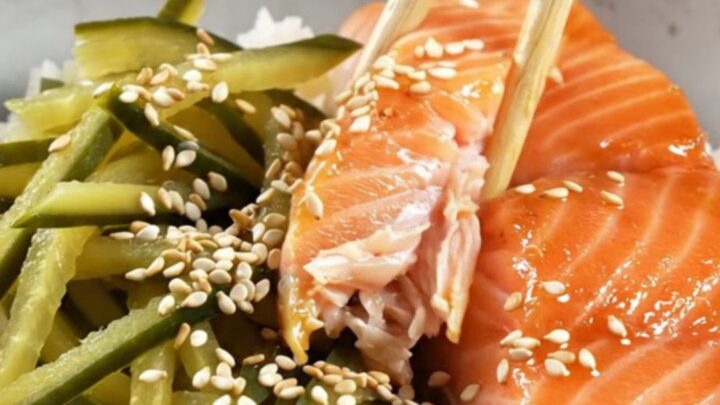 A bowl of teriyaki salmon with glossy glaze, pickled cucumber ribbons, and sesame seeds over rice