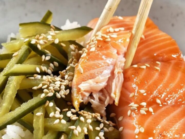 A bowl of teriyaki salmon with glossy glaze, pickled cucumber ribbons, and sesame seeds over rice