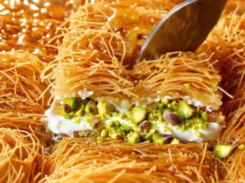 Golden kadayıf baklava with clotted cream and pistachios, drizzled with syrup on a copper tray.
