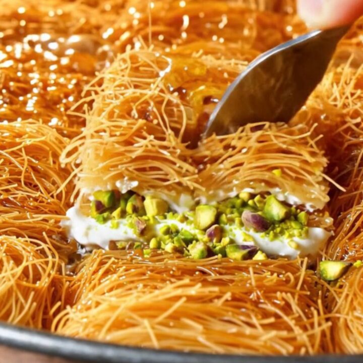 Golden kadayıf baklava with clotted cream and pistachios, drizzled with syrup on a copper tray.