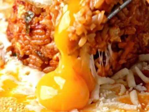 A cast iron skillet filled with red kimchi fried rice, surrounded by a bubbling moat of melted mozzarella cheese