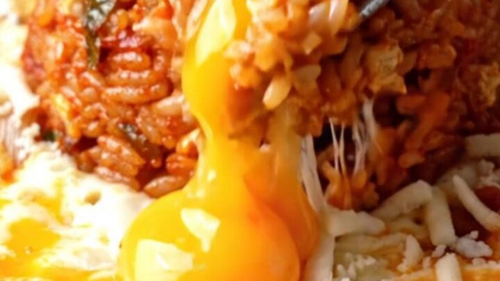 A cast iron skillet filled with red kimchi fried rice, surrounded by a bubbling moat of melted mozzarella cheese