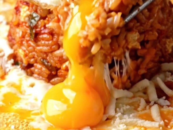 A cast iron skillet filled with red kimchi fried rice, surrounded by a bubbling moat of melted mozzarella cheese
