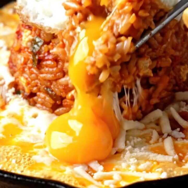 A cast iron skillet filled with red kimchi fried rice, surrounded by a bubbling moat of melted mozzarella cheese