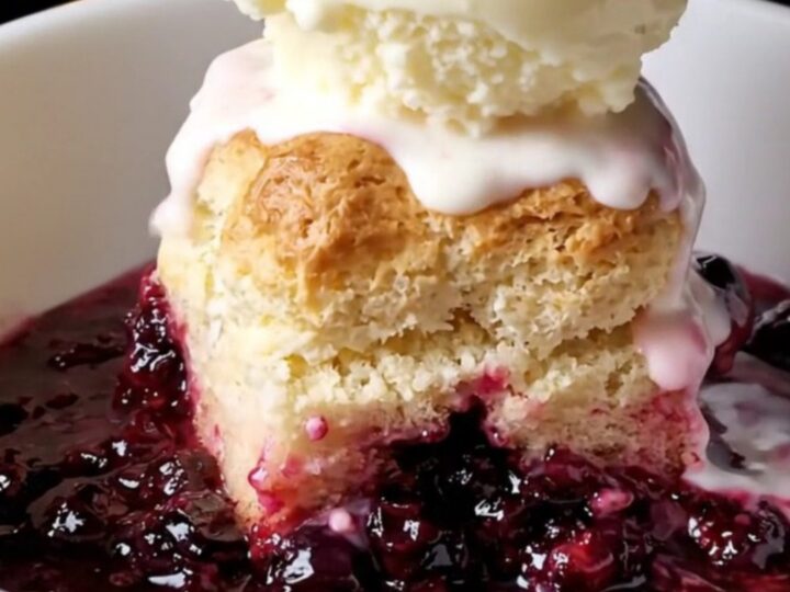 Cast iron skillet filled with bubbling blueberry cobbler topped with golden biscuits and melting vanilla ice cream