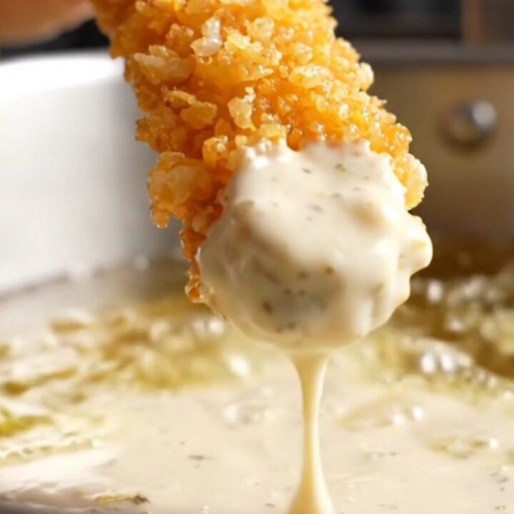 A metal spider holding golden crispy panko-crusted fried pickle chips, with a bowl of buttermilk ranch in the background.